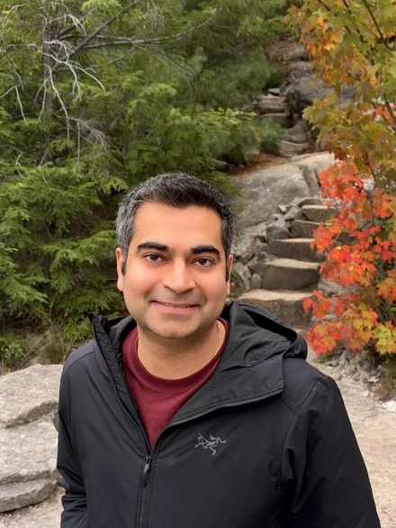 Sameet Sapra outdoors in autumn, red maple foliage behind him